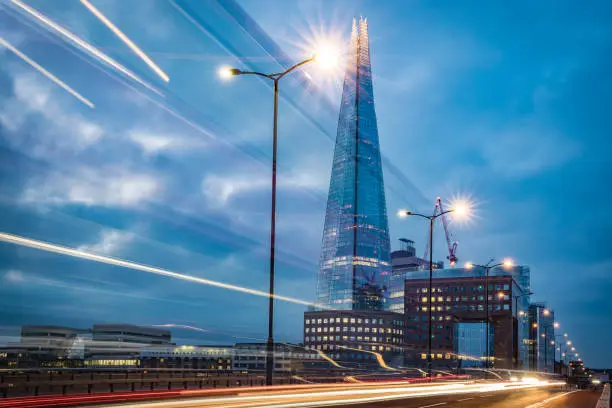 The Shard building in London city as photographed from London Bridge in the early morning hours with some blurred motion traffic and tail light trails. Shot on Canon EOS R full frame system.
