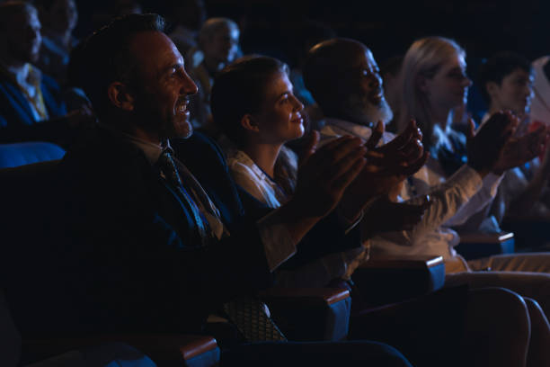 istock Business colleagues sitting and watching presentation with audience and clapping hands 1133973031