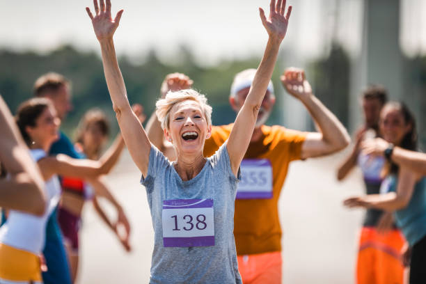 счастливый зрелый бегун приветствие ее сторонников во время марафонской гонки. - marathon jogging running finishing стоковые фото и изображения
