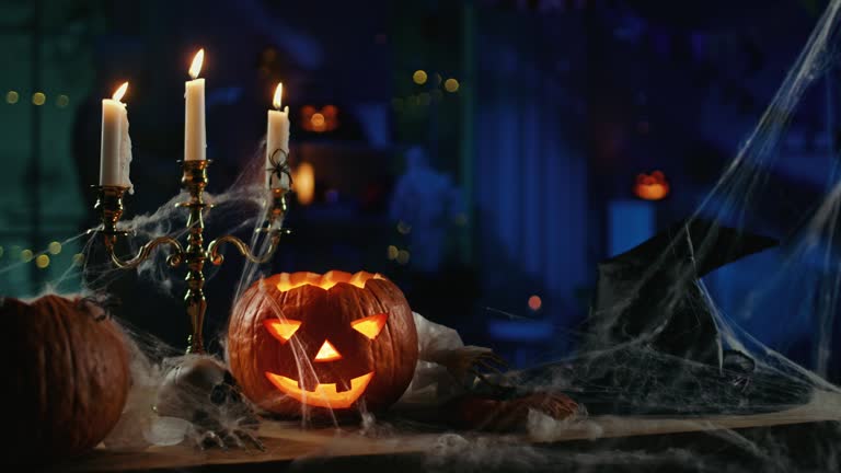 Halloween Still Life Colorful Theme: Scary Decorated Dark Room with Table Covered in Spider Webs, Burning Pumpkin, Candlestick, Witch's Hat and Skeleton. In the Background Silhouette of Monster Walking By