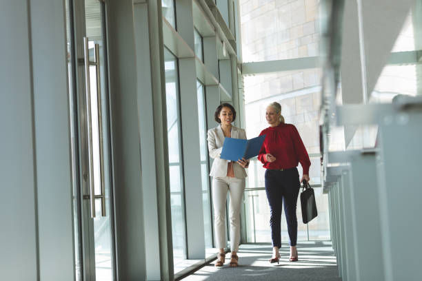 istock Businesswomen discussing over document while walking in office building 1133980219