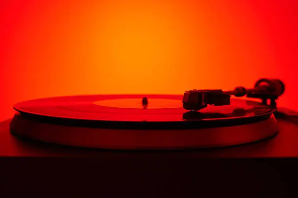Turntable vinyl record player in the red light. Needle on the plate. Sound technology for DJ to mix & play music. Light purple vinyl record