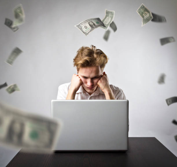 istock Young man using a laptop to browse the net. Young worker and falling dollar banknotes. Currency and job concept. 1133983622