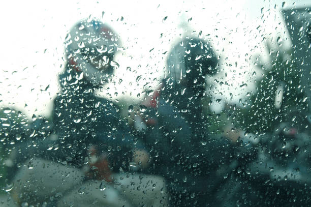 View of motorcycle riders in the rain through a window with rain drops