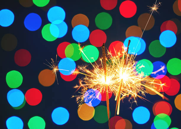 istock Holiday dynamic postcard. Two lighted fireworks on a blurred background of a bright Christmas garland. Meeting the new year. Christmas evening. Blur bottles on background 1133986775
