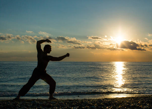 istock Single man does martial arts on the beach during sunset time. Wushu. 1133987609