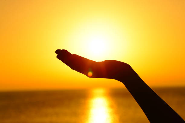 frau hält sonne bei sonnenuntergang am strand - catch light stock-fotos und bilder