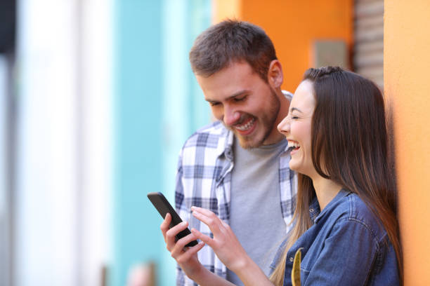 Happy couple laughing checking smart phone Happy couple laughing checking smart phone meme photos stock pictures, royalty-free photos & images