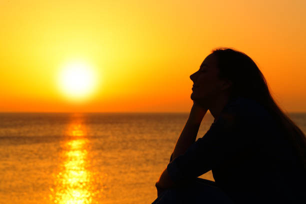 istock Woman silhouette watching sun at sunset on the beach 1133988062
