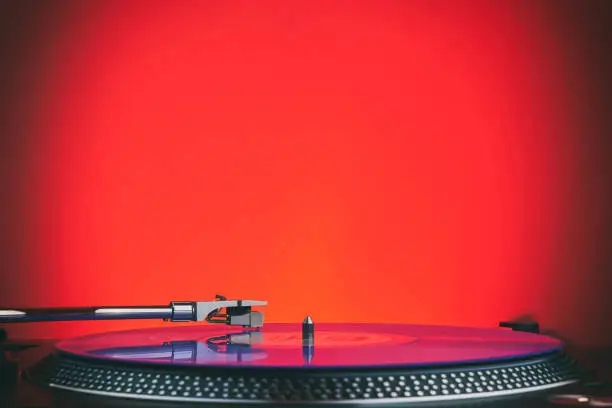 Turntable vinyl record player in the red light. Needle on the plate. Sound technology for DJ to mix & play music. Light purple vinyl record