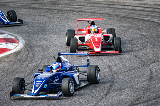 Men driving formula racing cars on motor racing track.