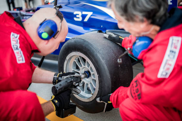 Racing team working at pit stop Pit crew in red uniforms changing tires on formula race car during pit stop. pitstop stock pictures, royalty-free photos & images