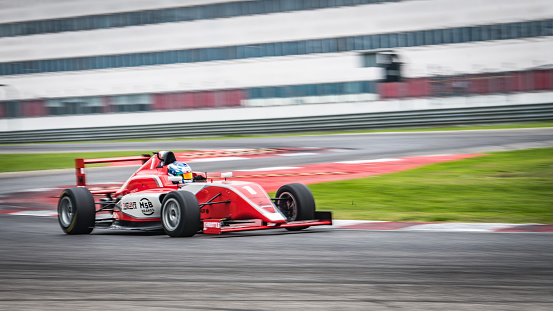 Blurred motion of man driving formula racing car on motor racing track.