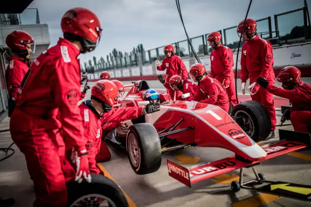 Pit crew in red uniforms changing tires on formula race car during pit stop.