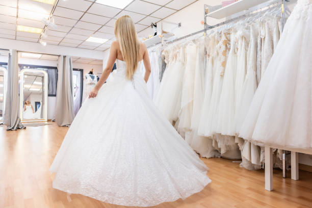 Rear view of bride in bridal shop Rear view of blonde bride in bridal shop in haute couture wedding dress. bridal shop photos stock pictures, royalty-free photos & images