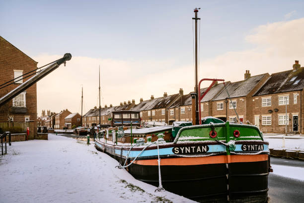 Vintage barges moored along the beck covered in snow, Beverley, UK. Beverley, UK - January 02. 2019: Vintage barges moored along the frozen beck (canal) and covered in snow flanked by town houses on January 02, 2019 in Beverley, Yorkshire, UK. sailboat mast stock pictures, royalty-free photos & images