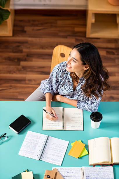 University student relaxing Smiling latin girl looking away while studying. Portrait of pensive college student looking away while studying alone at library. Young thinking woman taking notes at university. creative writing class stock pictures, royalty-free photos & images