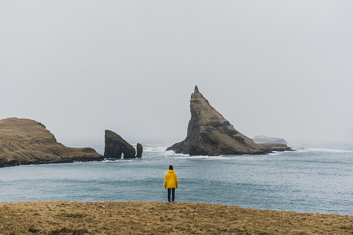 Woman in yellow raincoat looking at arch in Faroe Islands