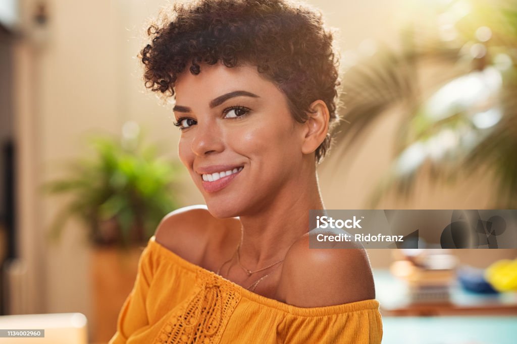 Smiling young african woman Portrait of natural beautiful girl smiling and looking at camera. Closeup face of brazilian young woman with curly hair. Charming african woman sitting at cafeteria. Women Stock Photo