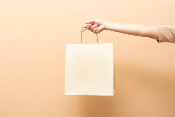 mano sosteniendo una bolsa de papel aislada en el fondo - paper bag fotos fotografías e imágenes de stock