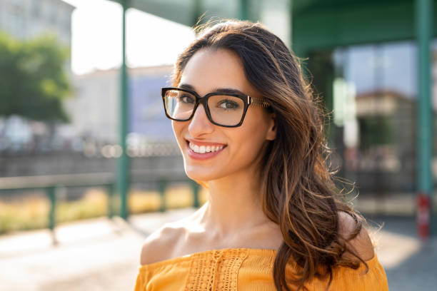 Smiling woman wearing eyeglasses outdoor Portrait of carefree young woman smiling and looking at camera with urban background. Cheerful latin girl wearing eyeglasses in the city. Happy brunette woman with long hair and spectacles smiling. brown hair stock pictures, royalty-free photos & images