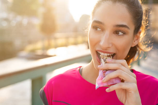 sportliche frau isst energieriegel - zwischenmahlzeit stock-fotos und bilder