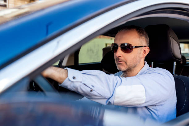 istock Man of style and status. Handsome young man in full suit smiling while driving a car 1134004054
