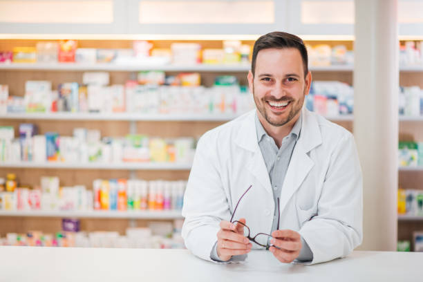 retrato de un farmacéutico guapo y alegre apoyado en el mostrador en la farmacia. - 5949 fotografías e imágenes de stock