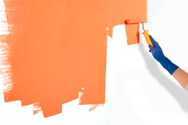 istock Worker painting white wall orange with paint roller 1134018540