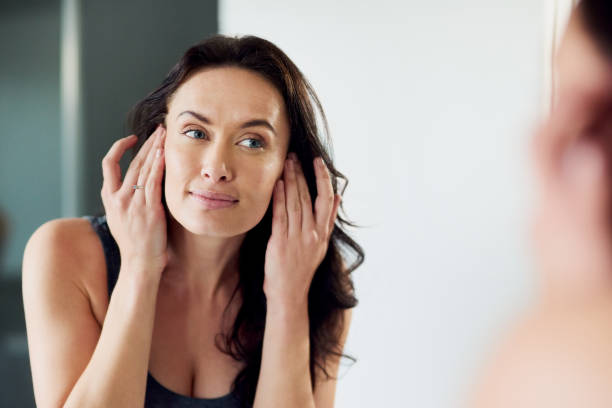 Her skin has never been healthier Cropped shot of an attractive woman admiring her face in the bathroom mirror smooth stock pictures, royalty-free photos & images