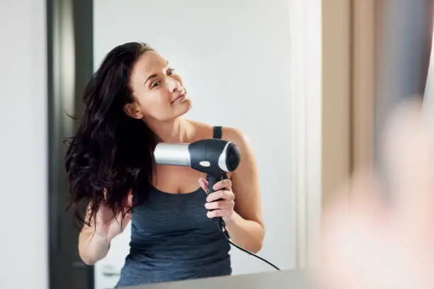 Cropped shot of an attractive woman blowdrying her hair in front of a mirror in the bathroom
