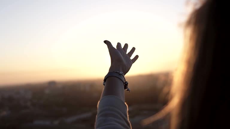 Woman with smart watches touching the sunlight by hand over beautiful sky background while standing on the roof. Happy woman looking at sunrising through his fingers and waving her hand. Slow motion