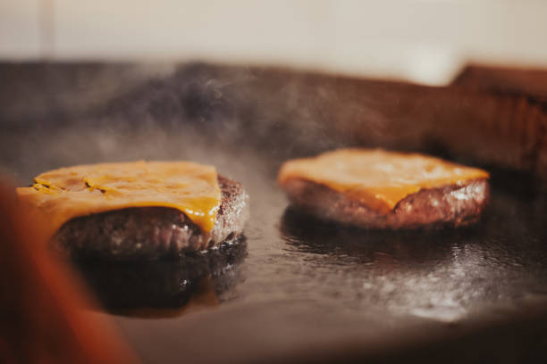 Cheeseburgers frying on the grill while smoke going up