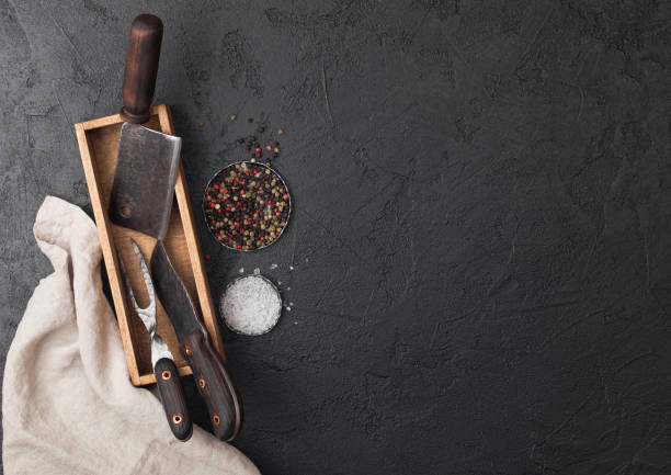 istock Vintage meat knife and fork and hatchet in old wooden box on black table background. Butcher utensils. Space for text 1134022708