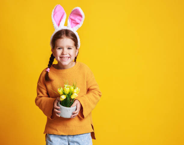 イースターバニー耳と黄色の春の花チューリップとおかしい幸せな子供の女の子 - easter egg easter yellow paint ストックフォトと画像