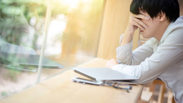Overworked Asian businessman feeling stressed and tired from business problem while working with laptop computer in cafe. Migraine symptoms or headache from work failure.