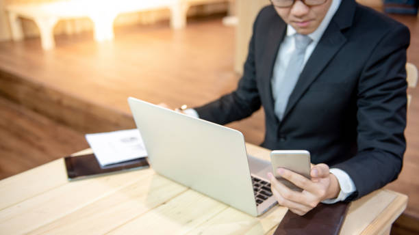 istock Asian businessman wearing black suit using modern smartphone while working with digital tablet, laptop computer and report paperwork on the table at office. Mobile app or mobile application concepts 1134039355