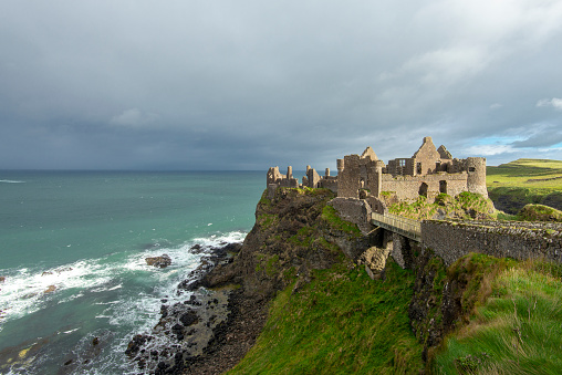 Sunlight and a dramatic sky over the ruins of medieval Dunluce Castle on a steep cliff, Northern Ireland.