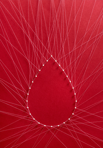 Donate blood concept. Network of pins and threads in the shape of a blood drop symbolising group effort and collaboration for saving lives.
