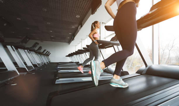Low section of female runner running on treadmills at gym.