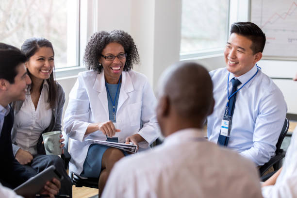 Cheerful medical coworkers enjoy staff meeting A group of cheerful medical coworkers sit in a circle for a staff meeting.  They laugh together as they talk. hospital card stock pictures, royalty-free photos & images