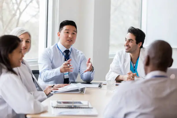 Young male hospital administrator gestures while discussing a topic with doctors and other people in hospital management.