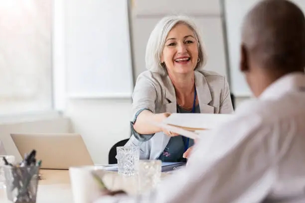 Smiling female hospital administrator hands a document to a mature male doctor.