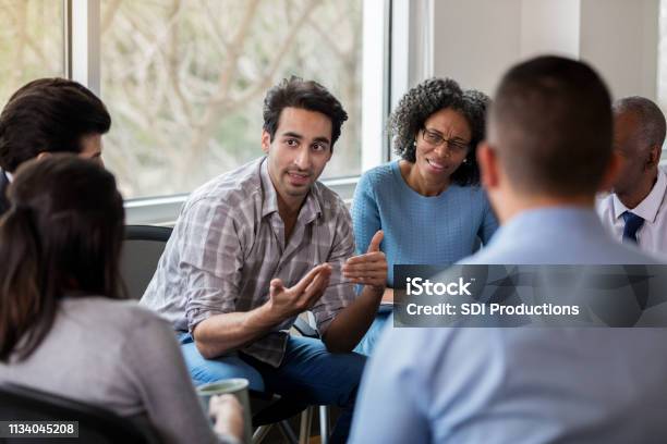 Mid Adult Businessman Gestures During Meeting Stock Photo - Download Image Now - Group Of People, Discussion, Group Therapy