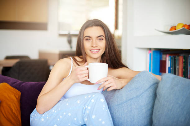 istock Beautiful young woman holding mug in her hand while relaxing on sofa at home 1134045430