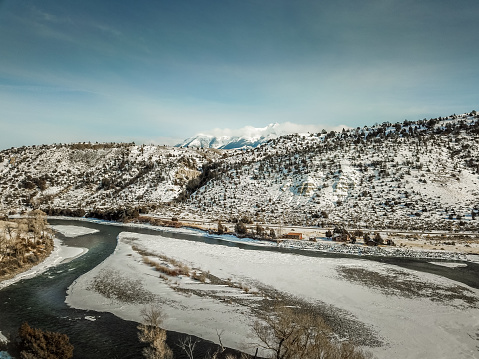 An aerial view of the Yellowstone River in Montana as the sun starts to set. The river winds its way past the mountains that are covered in snow.  Parts of the Yellowstone River are frozen.