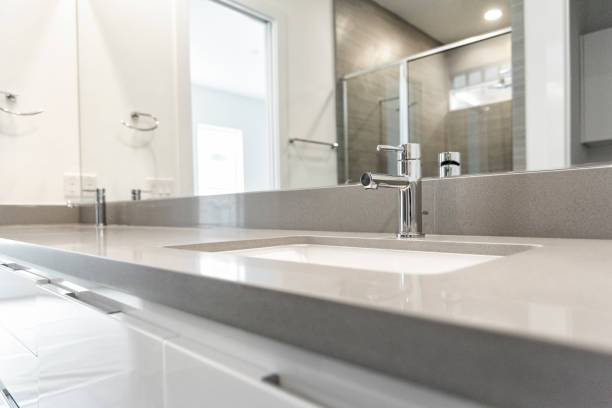 Wide angle view of this new bathroom counter including sinks, cabinets, and mirror with the reflection of the newly installed shower in the reflection.