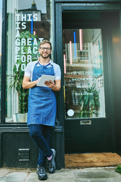 Taking the time to do some thinking Portrait of a cheerful young waiter standing with his notebook and pen ready to take orders outside of a coffee shop during the day small business saturday stock pictures, royalty-free photos & images