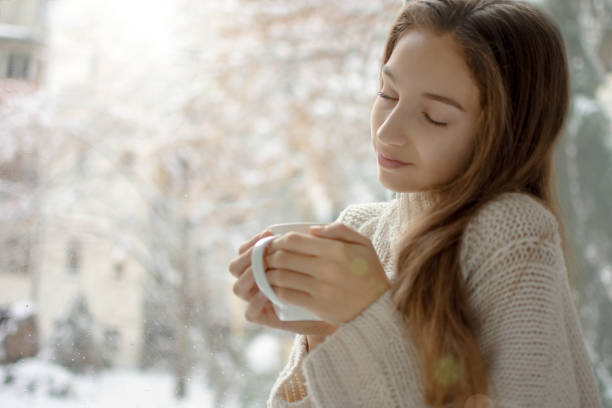istock Young woman enjoys drinking coffee by window 1134054526
