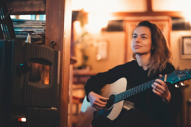 Young woman playing guitar close up indoors in low light.Playing guitar. Young teeanger playing guitar by herself. stock photo